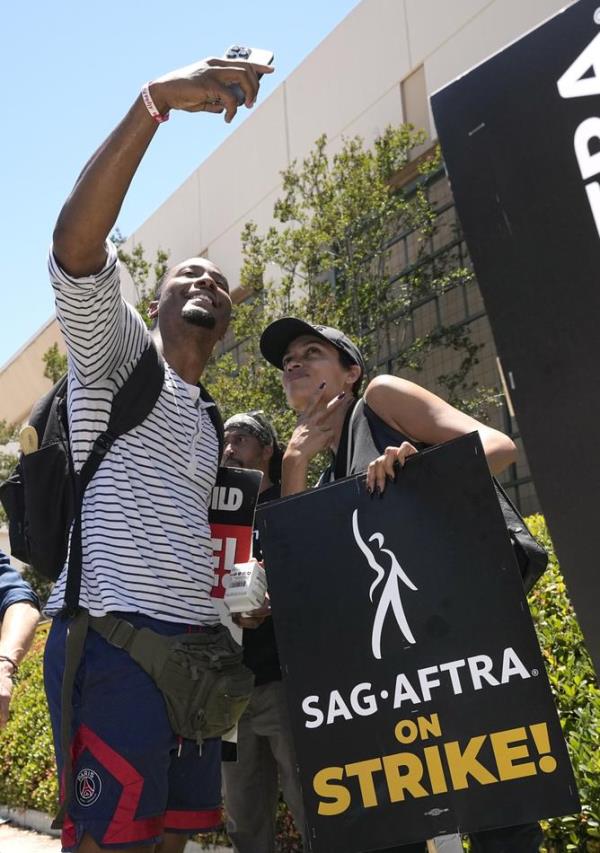 Actor Rosario Dawson, right, takes a selfie at rally with a fellow participant at a picket line outside Warner Bros. studios.
