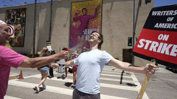 Luke DePalatis, right, gets a cooling spritz of water from Michael Abel during a rally by striking writers and actors outside Warner Bros. studios.